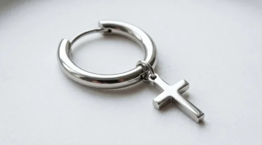 Boucle d'oreille créole en acier inoxydable avec pendentif croix capturant la lumière sur une surface blanche